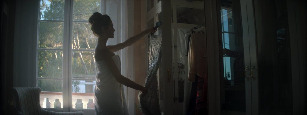 Sweet Matitos fashion film still: a model taking a dress out of the wardrobe, against the light from the window