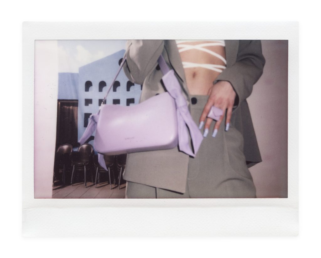 Blame Lilac Poderío: Instax of a lilac bag with a bow against a gray suit