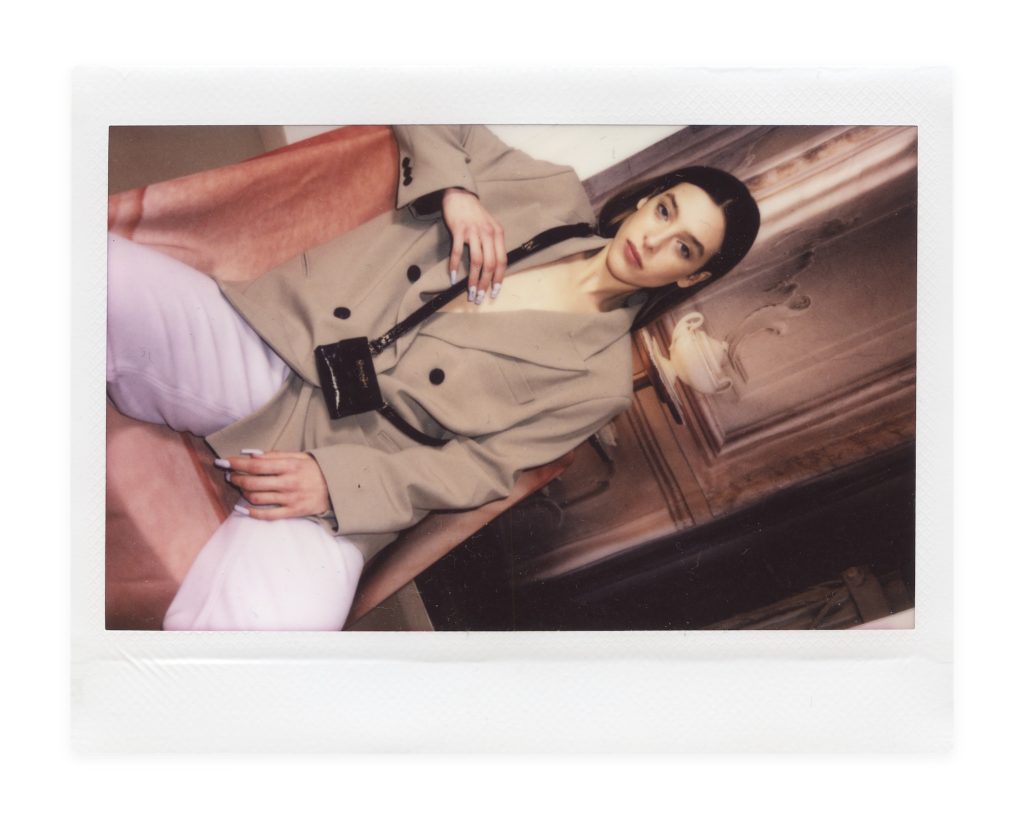 Blame Lilac Poderío: Instax of the model in an armchair in a beige suit with a small black bag