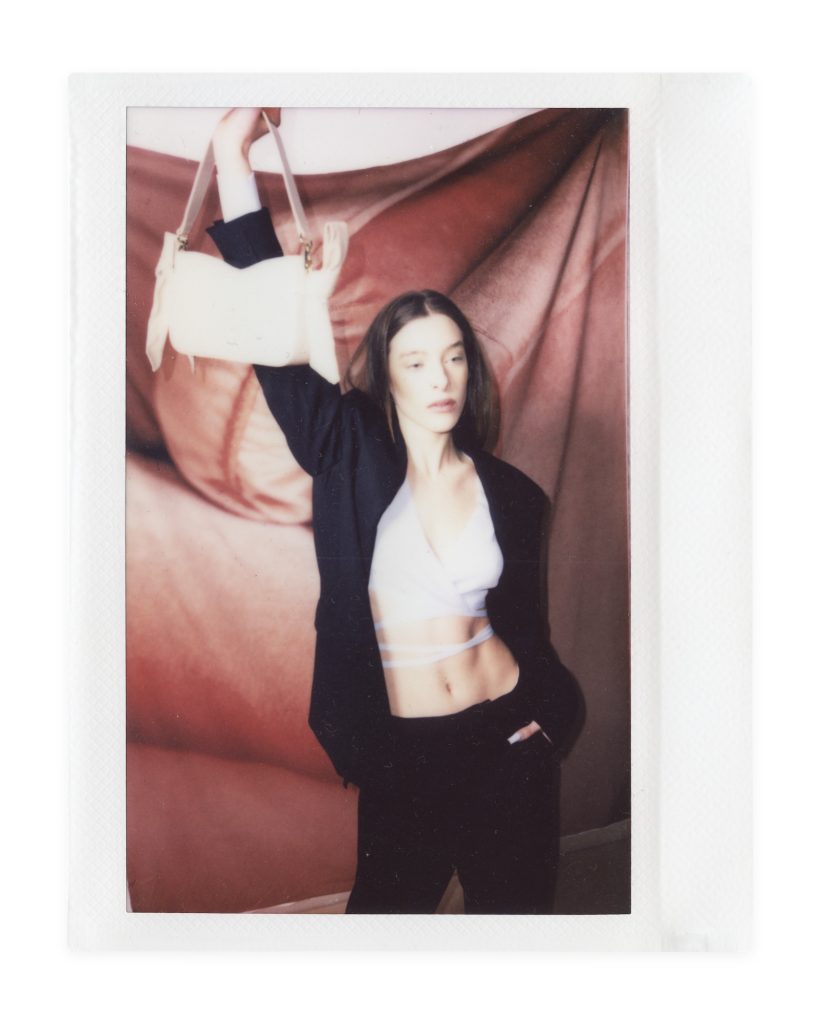 Blame Lilac Poderío: Instax of the model in a black suit holding up a cream bag