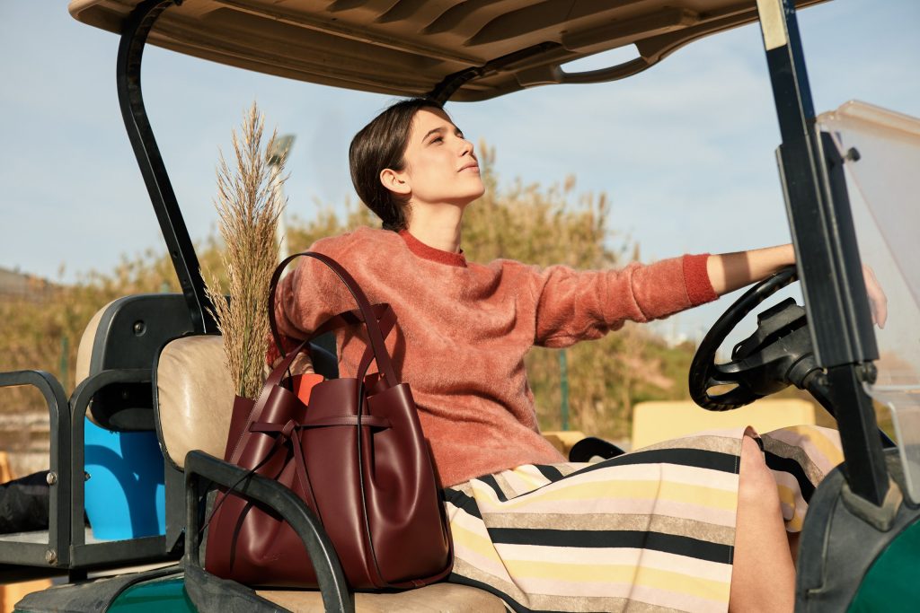 Boria&Coria: model in a red sweater with a burgundy bag in a golf cart