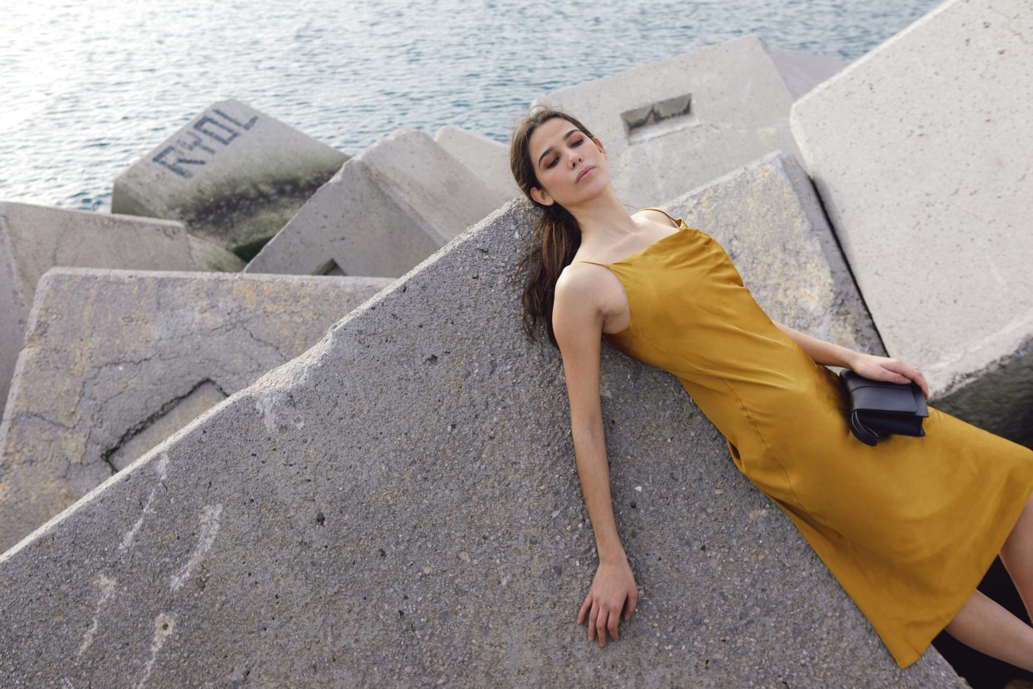 Boria&Coria: model in a yellow dress lying on concrete blocks by the sea