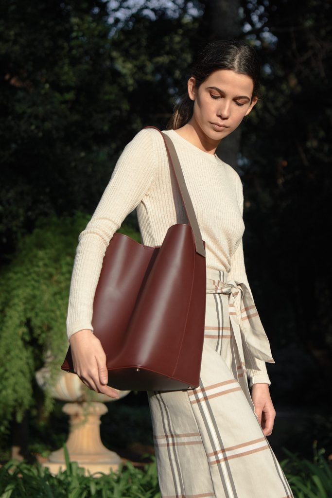 Boria&Coria: model with a burgundy bag on her shoulder in a garden