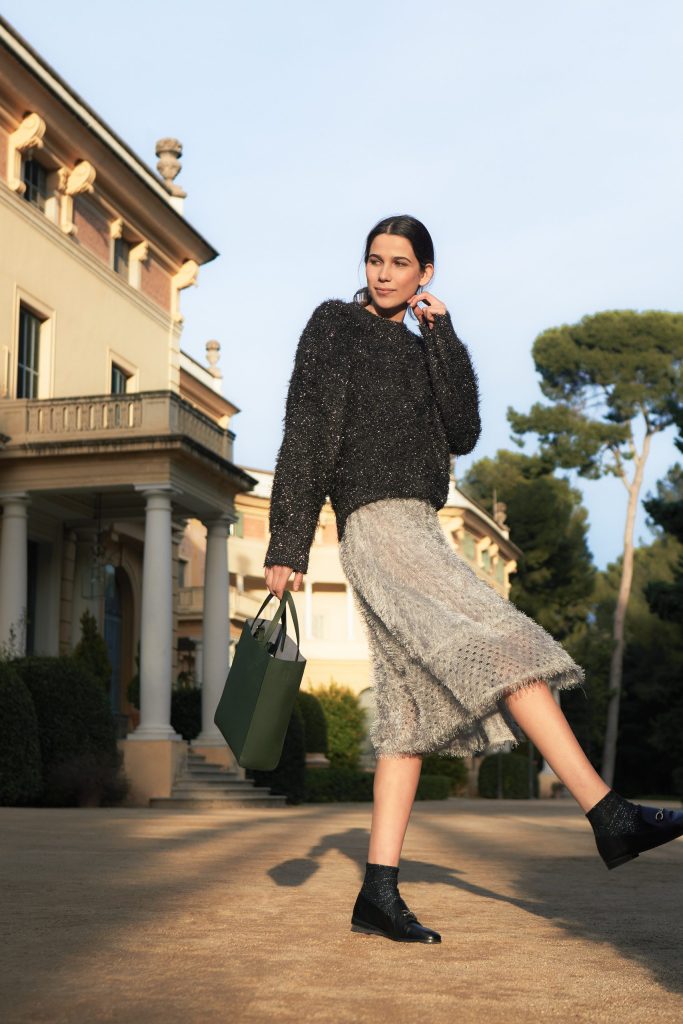 Boria&Coria: model in a gray sweater with a green bag walking in front of a villa