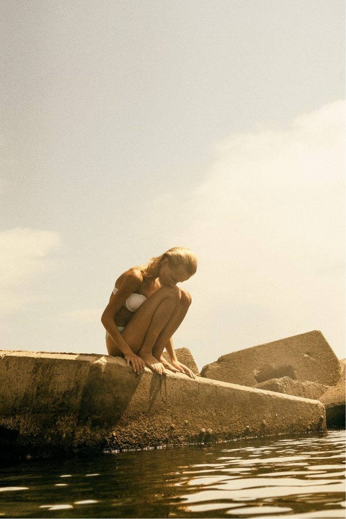 Grain Supply: model crouching on a concrete block by the water