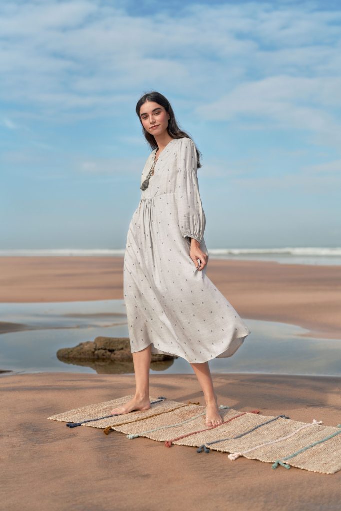 marwa: model in a white dress on a woven mat on the beach