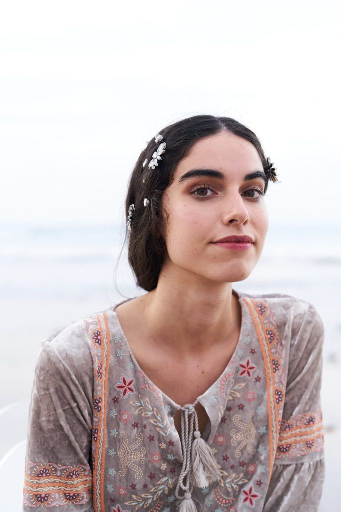 marwa: close-up of the model with flower pins in her hair and an embroidered velvet dress, with the misty shore behind